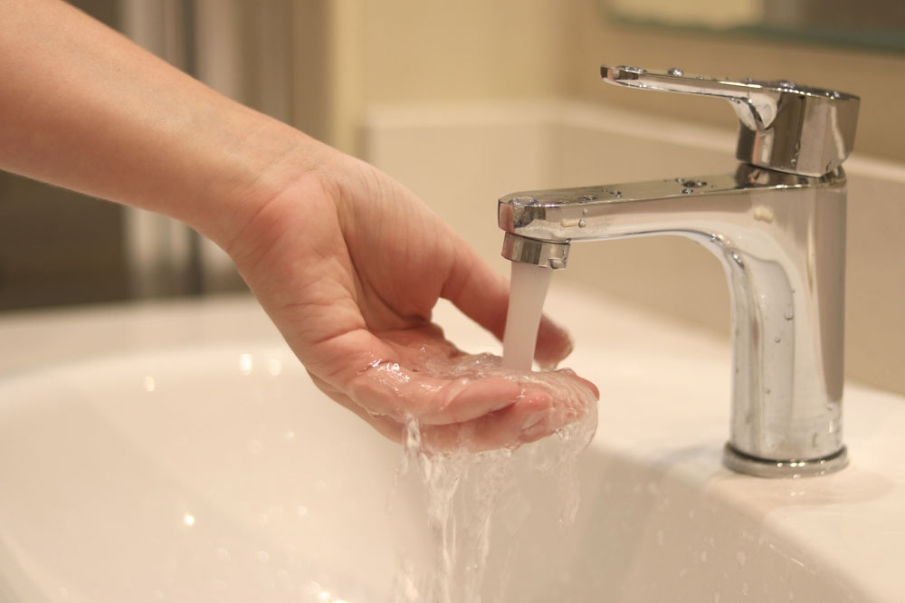 hand placed underneath a faucet (checking for water flow)